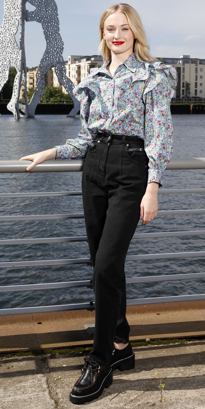 Sophie Turner pairs a floral-embellished blouse with high-waisted black jeans and chunky lace-up boots at an X-Men: Dark Phoenix photocall in Berlin on May 20, 2019, using substantial footwear to ground the romantic silhouette