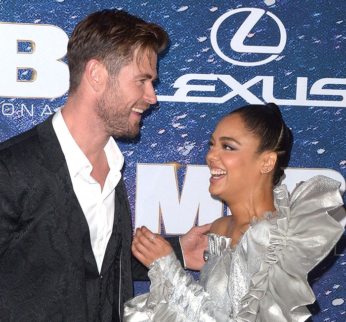 Chris Hemsworth and Tessa Thompson share a laugh on the red carpet at the Men in Black: International premiere, with Tessa stunning in her dramatic silver Rodarte gown featuring oversized ruffles and a one-shoulder design