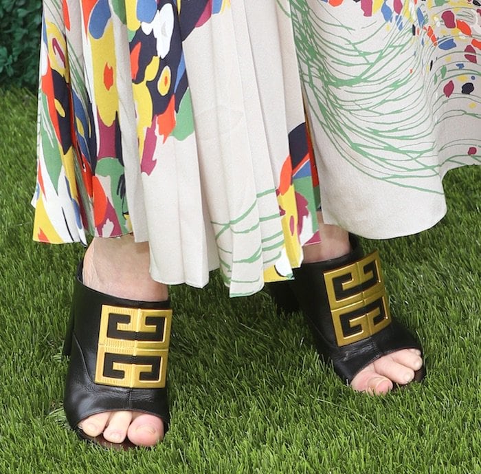 A close-up highlights her black leather Givenchy slides, topped with the iconic gold 4G plaque and set on a sturdy block heel perfect for navigating turf
