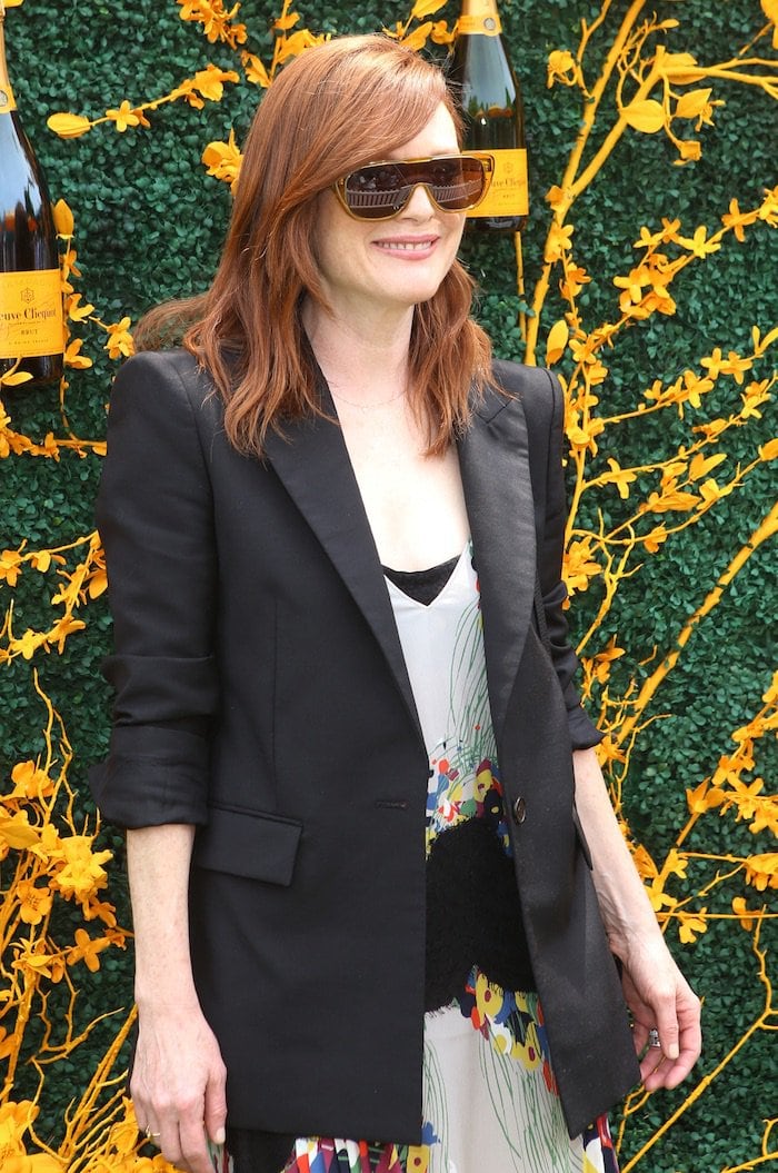 Julianne Moore layered a sharp black blazer over a colorful pleated Givenchy midi dress, accessorizing with oversized sunglasses against the Veuve Clicquot floral backdrop