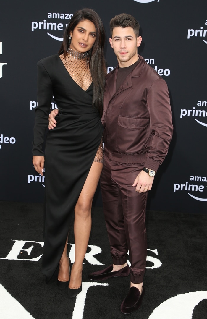 Priyanka Chopra's sleek black pumps grounded the sculptural Galia Lahav design, while Nick Jonas complemented her sophisticated evening look in a satin-finish brown jacket, matching trousers, and velvet loafers