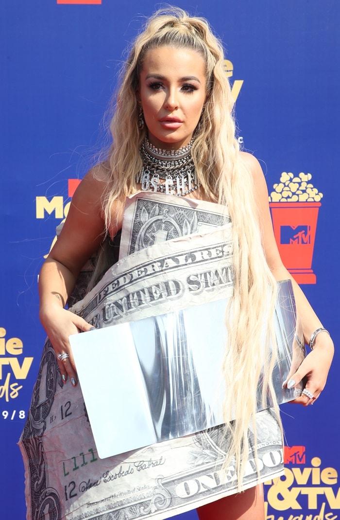 The oversized metallic money clip and sharply pointed chrome heels gave Tana Mongeau’s novelty-print mini dress a harder, industrial edge at the Barker Hangar in California