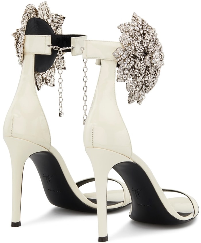 Giuseppe Zanotti’s Fleur sandals in white patent leather pair a sleek stiletto frame with an oversized crystal flower at the ankle for a high-contrast, sculptural finish