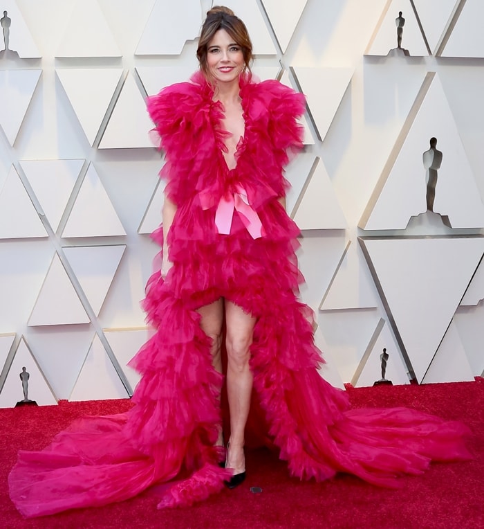 Linda Cardellini lets sharp black pumps cut through the drama of her vivid Schiaparelli couture gown, using the pointed silhouette to ground the feathered volume with precision