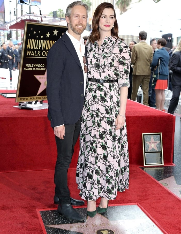 Anne Hathaway is joined by her husband, Adam Shulman, at her Hollywood Walk of Fame star ceremony on May 9, 2019, wearing a romantic Valentino Fall 2019 floral dress styled with classic Jimmy Choo “Anouk” green suede pumps for a polished, celebratory finish