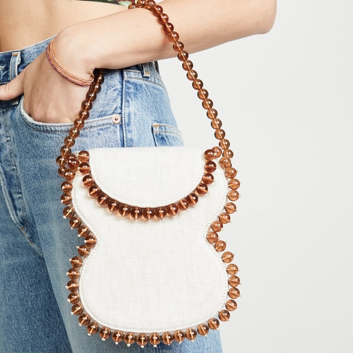 Off white envelope bag with a foldover top with snap closure, an internal slip pocket, and a beaded top handle and trim
