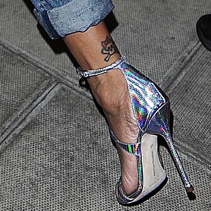 Rihanna highlights her delicate skull ankle tattoo in iridescent holographic sandals, the slim ankle strap and towering stiletto heel catching the light while framing the playful ink and her softly polished toes
