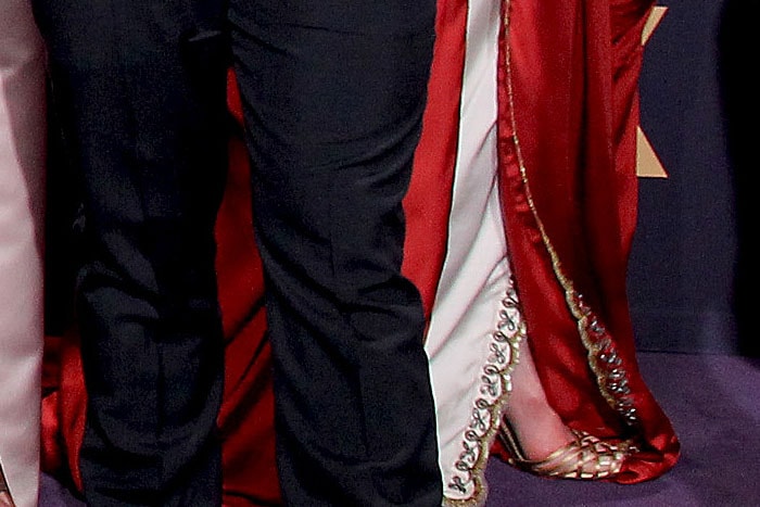 A close-up reveals Gwendoline Christie’s gold metallic Gucci sandals, their delicate crisscross straps peeking out beneath the dramatic hem of her custom gown