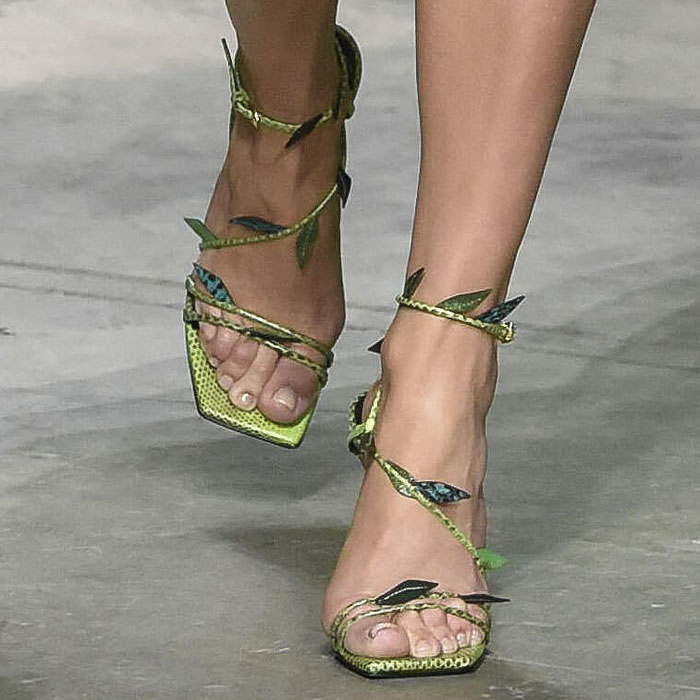 A close-up of Jennifer Lopez's custom Versace sandals reveals textured green snakeskin leather, sculptural leaf appliqués wrapping around the ankle straps, square toes, and slender stiletto heels inspired by the jungle motif