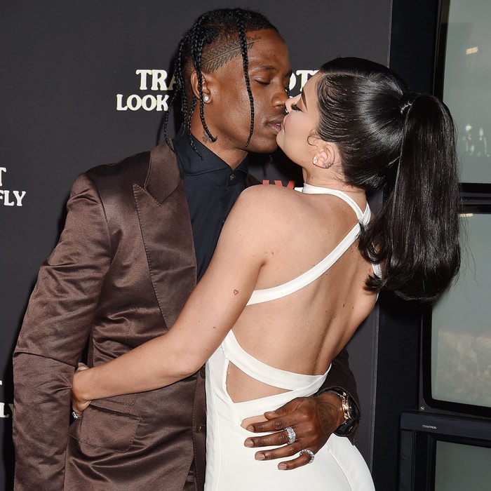 Kylie Jenner, nearly matching Travis Scott's height thanks to her high heels, stuns in a backless white gown while the couple shares a kiss at the premiere