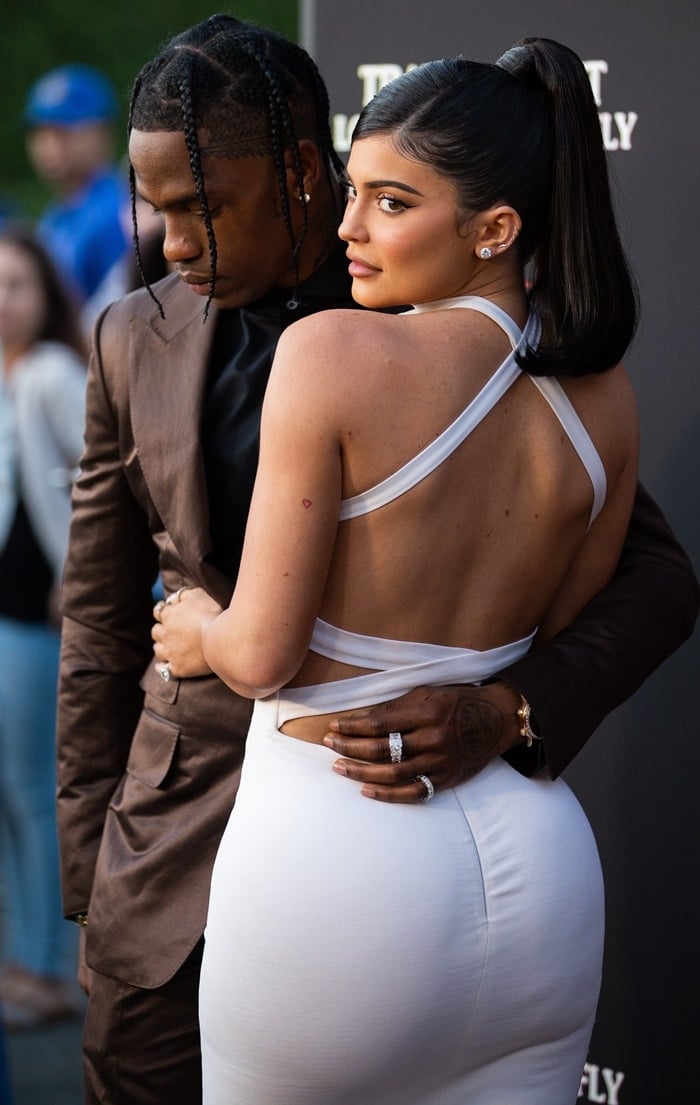 Kylie Jenner stuns in a backless white dress while Travis Scott complements her look in a sleek brown suit