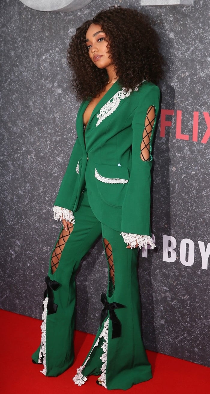 Leigh-Anne Pinnock wears an emerald-green Ana Ljubinković Fall 2019 pantsuit featuring white floral lace trim, corset-style cutouts, black bows, and dramatically split trouser legs