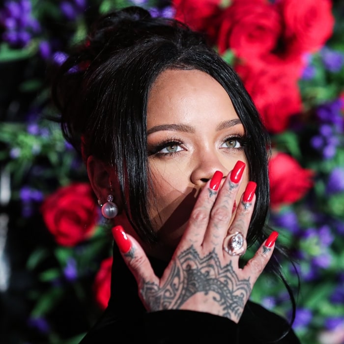 Rihanna’s glossy red manicure, pearl earrings, and intricate hand tattoos added sharp contrast to the sleek severity of her high-neck Givenchy couture look
