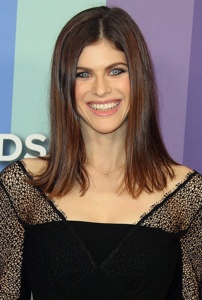Alexandra Daddario's hair is styled in sleek, straight layers with a center part, perfectly framing her striking blue eyes, which are highlighted with subtle eyeliner and a soft shimmer