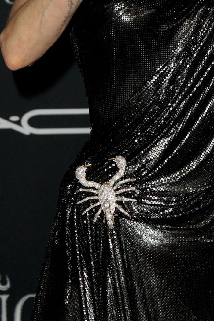 A crystal-embellished scorpion brooch cinches the gown at the waist, adding a symbolic, almost venomous edge to the sleek silhouette