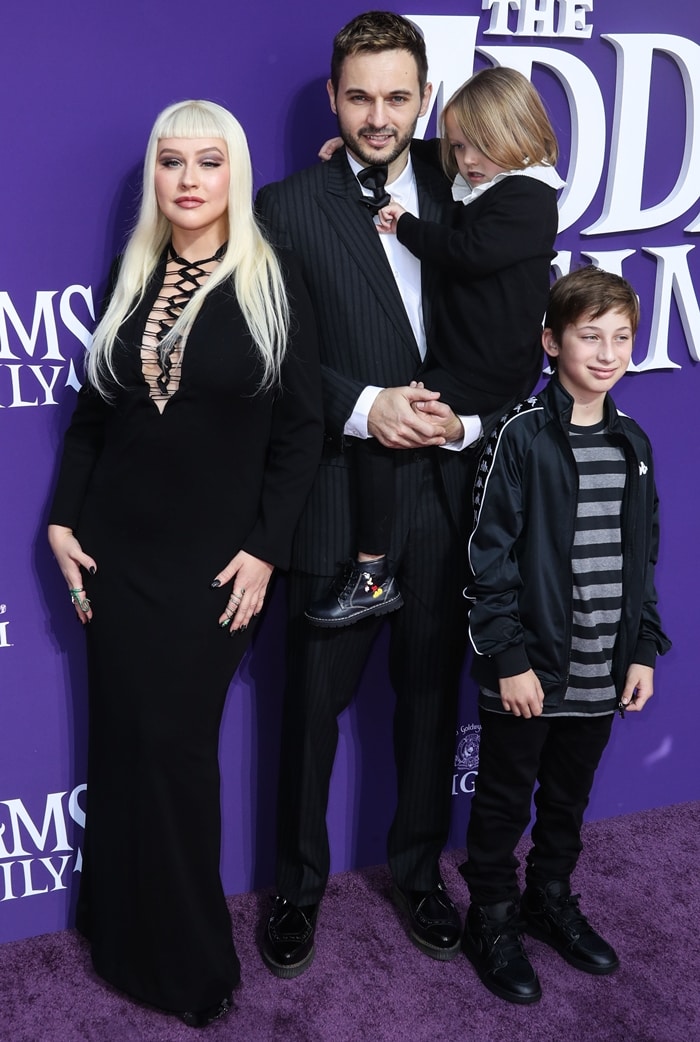 Christina Aguilera channels Morticia Addams in a long black lace-up gown and platform heels, posing with fiancé Matthew Rutler and their children, Summer Rain and Max Bratman, at The Addams Family premiere