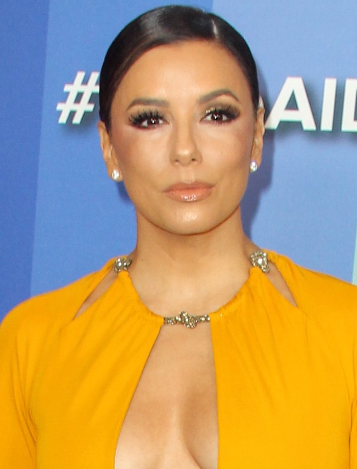 Eva Longoria's hair is styled in a sleek, polished low bun, perfectly highlighting her sparkling diamond stud earrings