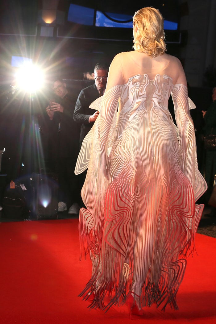 From behind, the dress reveals Iris van Herpen's intricate layered construction, with flowing laser-cut lines cascading into a crimson gradient that mirrors the movement of floating ink