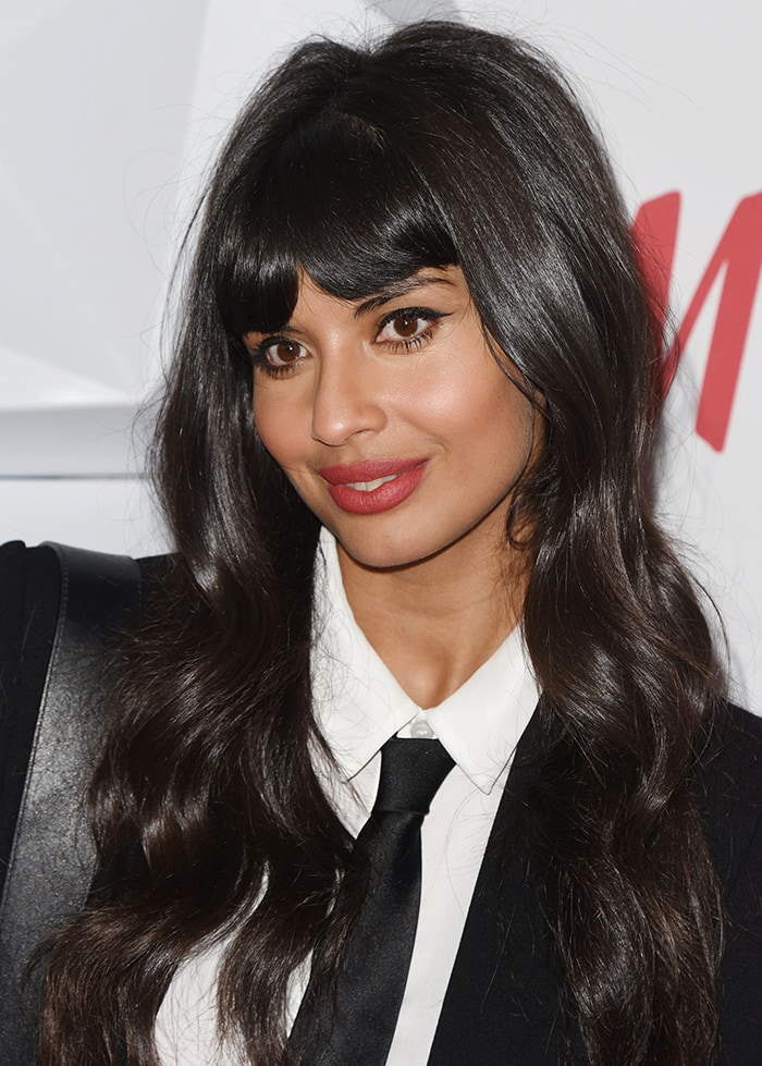 Jameela Jamil wears red lipstick and dark eye make-up, and styles her long black fringe hair in soft waves