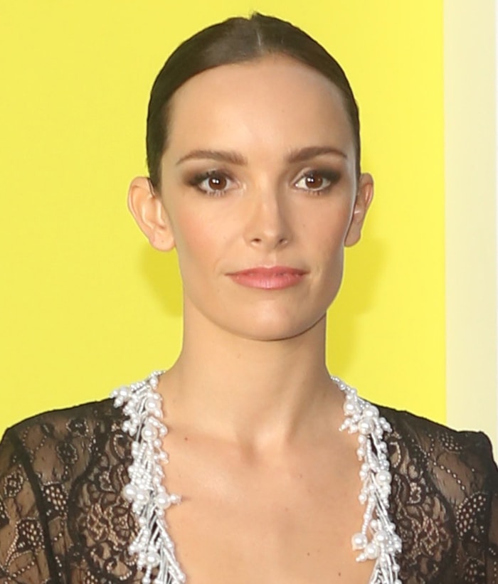 A beauty close-up highlights Jodi Balfour’s sleek center-parted bun, smoky eye makeup, and pearl-trimmed neckline, underscoring the delicate contrast between the lace bodice and soft pink skirt
