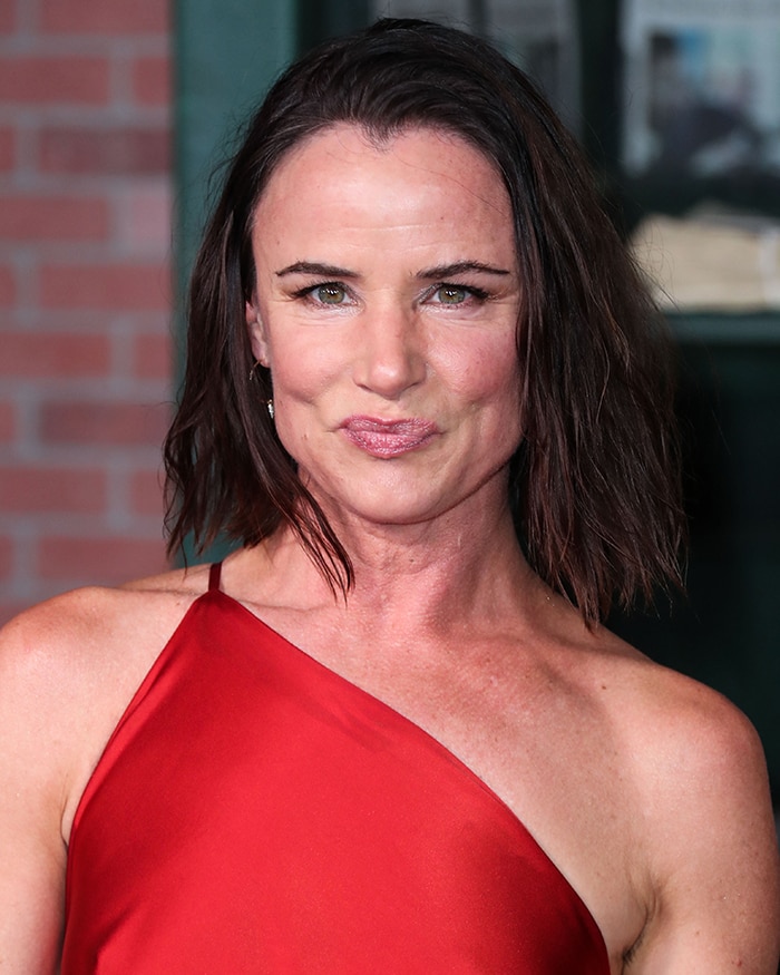 Juliette Lewis embraces an undone glam aesthetic with a wet-look bob, shimmering eyeshadow, and glossy pink lipstick against the sleek red satin dress