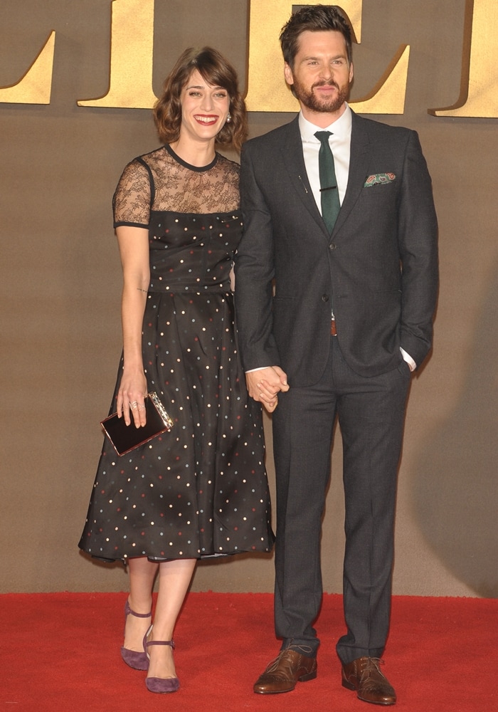 Lizzy Caplan and Tom Riley attend the UK premiere of Allied, with Lizzy wearing a playful polka-dot dress featuring lace details and Tom looking sharp in a tailored suit with a green tie and pocket square