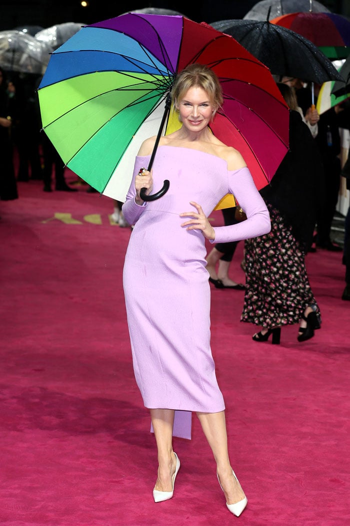 Renée Zellweger stayed polished in a lilac off-the-shoulder Emilia Wickstead dress, grounding the look with white patent Christian Louboutin “So Kate” pumps that cut a sharp, leg-lengthening line despite the rain at the European premiere of Judy at Curzon Mayfair in London on September 30, 2019