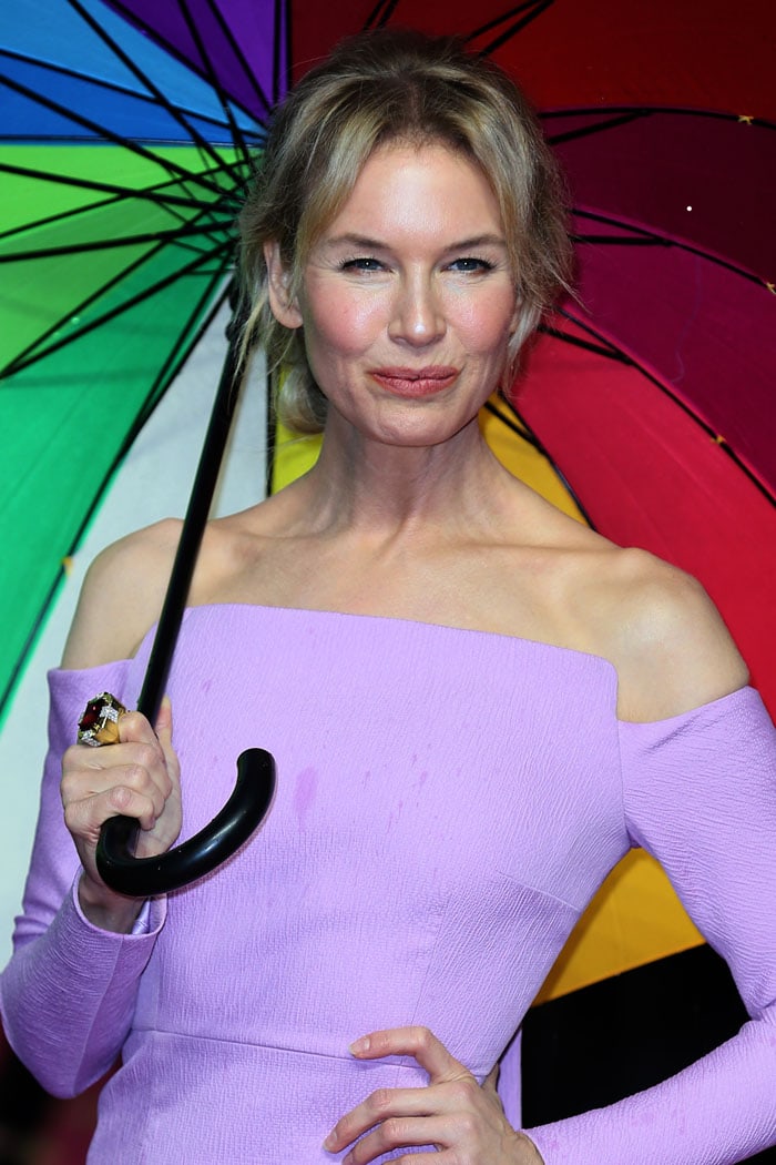 Renée Zellweger brightened a rain-soaked London premiere with a lilac off-the-shoulder Emilia Wickstead dress, framed by a rainbow umbrella that added a graphic burst of color to the red carpet