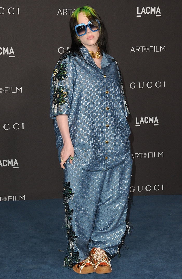 Billie Eilish hit the carpet in a teal embroidered Gucci set with fringe floral appliqués, pairing the oversized silhouette with crystal-studded Gucci Flashtrek sneakers for a fully maximalist moment
