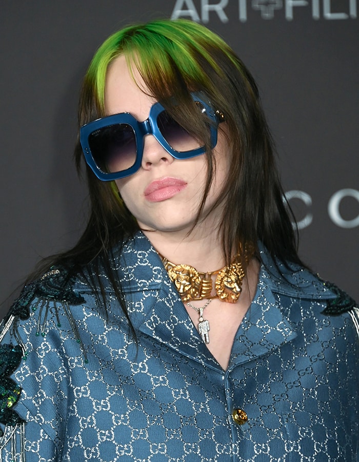 Leaning into her bold aesthetic, Billie finished the look with electric blue oversized sunglasses, her signature neon-green roots, and a chunky gold Gucci lion-head necklace