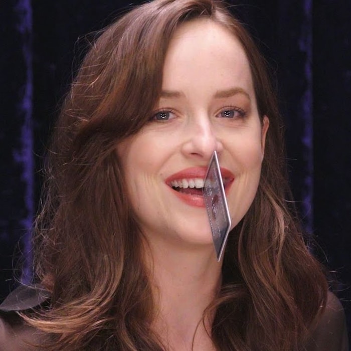Dakota Johnson demonstrates her once-famous tooth gap by playfully holding a credit card between her front teeth during a Vanity Fair interview