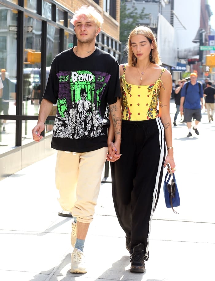 Dua Lipa pairing a printed corset-style top and striped track pants with chunky black sneakers and a cobalt-blue handbag for an effortless off-duty look