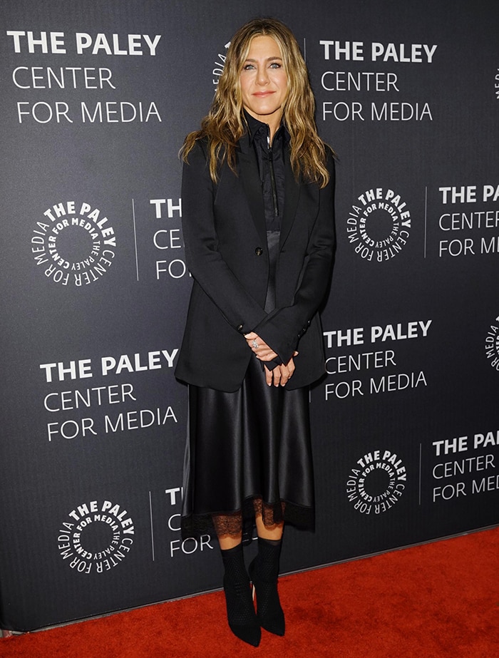 Jennifer Aniston opts for an all-black tailored look, anchoring her ensemble with a structured jacket and fluid satin skirt