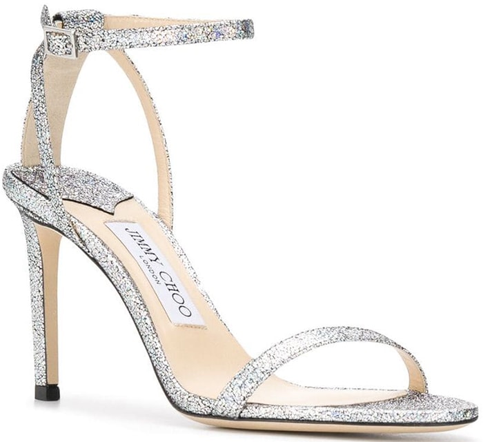 The Jimmy Choo “Minny” sandals feature slim glittering straps, an ankle buckle, and a slender stiletto heel designed for evening wear