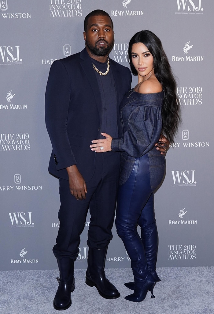 Kim Kardashian and Kanye West embrace coordinated Burberry dressing at the 2019 WSJ Magazine Innovator Awards, with Kim pairing indigo leather-paneled denim and matching lace-up stiletto boots while Kanye complements her monochromatic palette in a navy suit and oversized galoshes