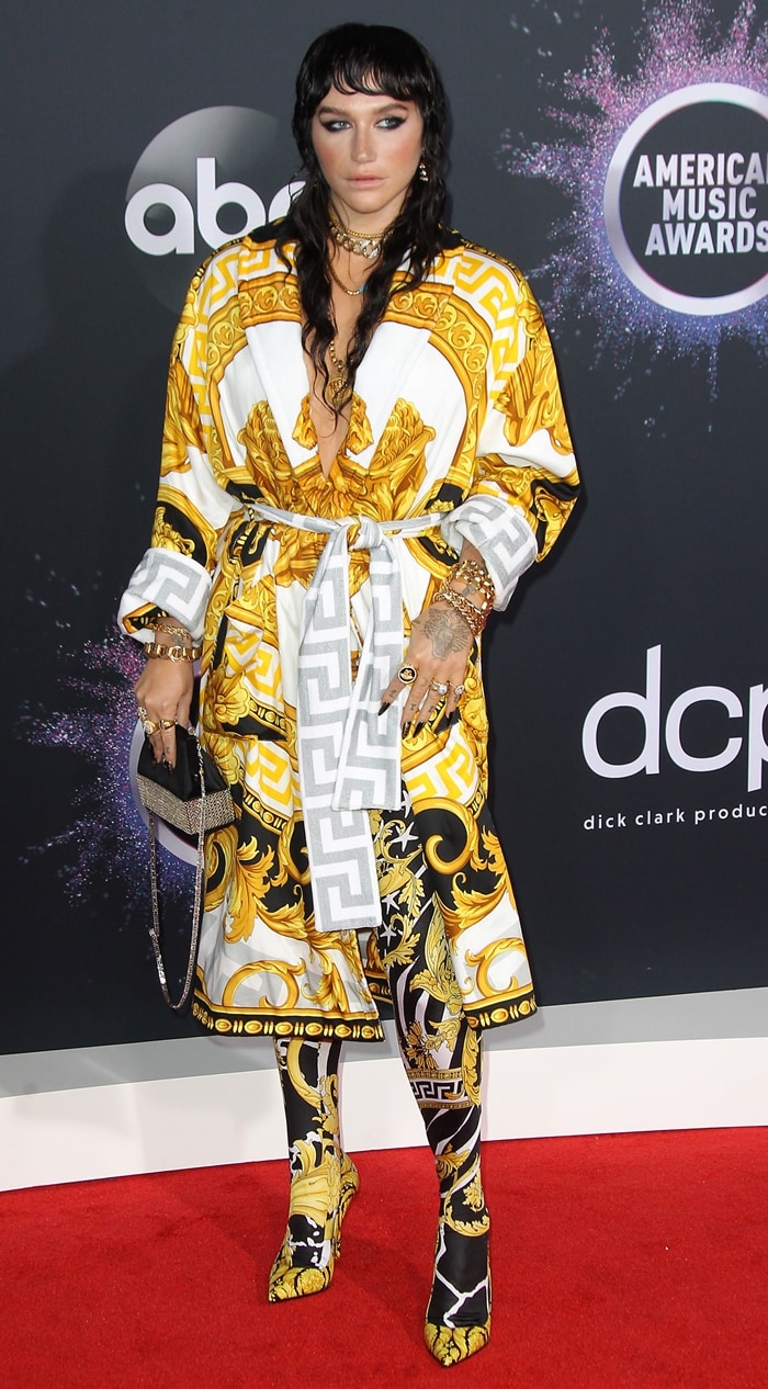 Kesha embraces full head-to-toe Versace styling with ornate printed leggings, a crystal-trimmed clutch, and matching archival-inspired accessories