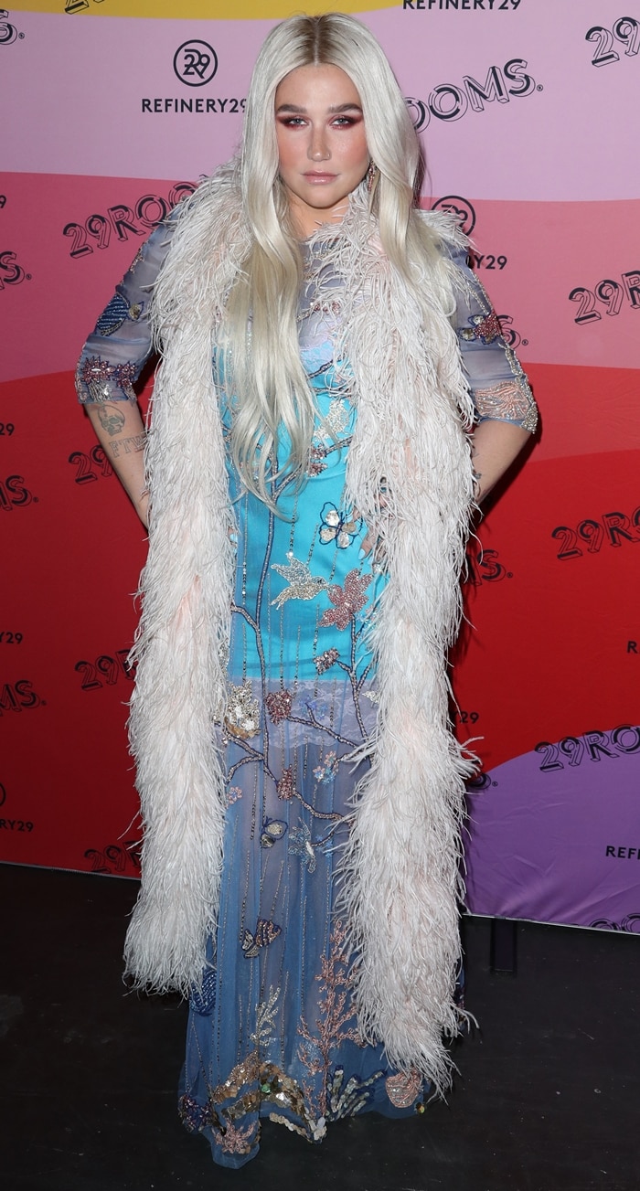 Kesha layers a feathered white boa over a sheer embroidered gown at Refinery29’s 29Rooms event, blending bohemian glamour with theatrical red carpet styling