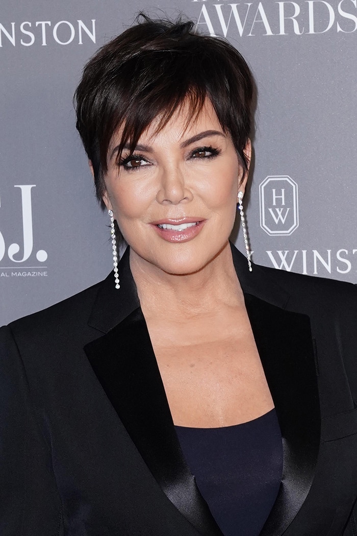 Kris Jenner wears her pixie haircut with dark eyeliner, mascara, nude lip gloss, and diamond drop earrings