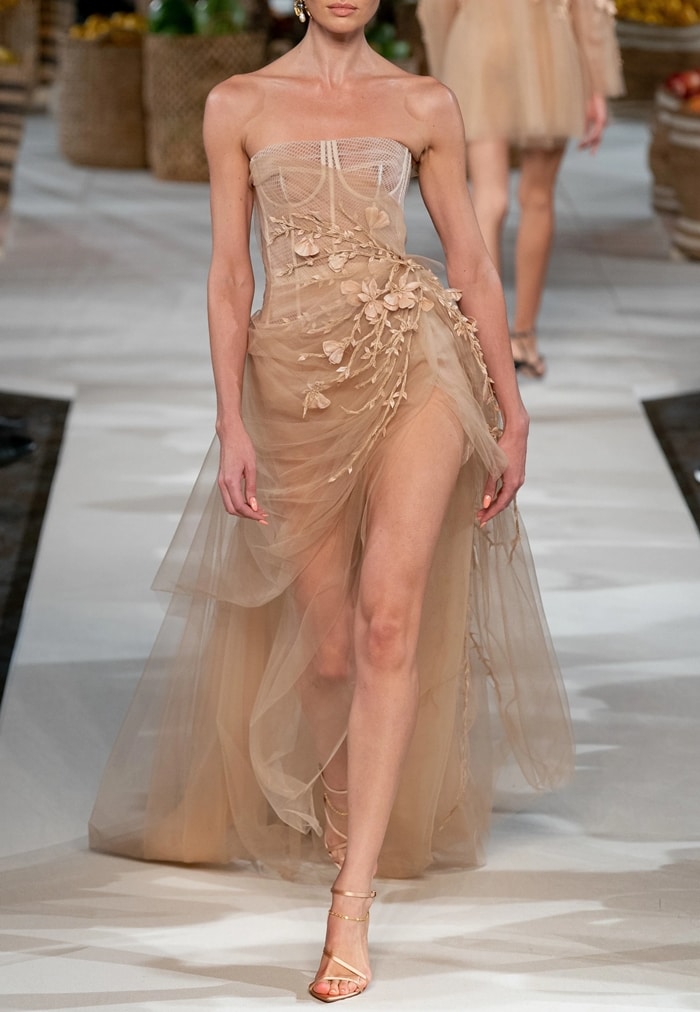 A runway model wears Camila Cabello's nude strapless Oscar de la Renta Spring 2020 gown, featuring draped tulle and floral appliqué detailing, styled with barely-there strappy sandals that highlight the dress’s airy, sculptural silhouette