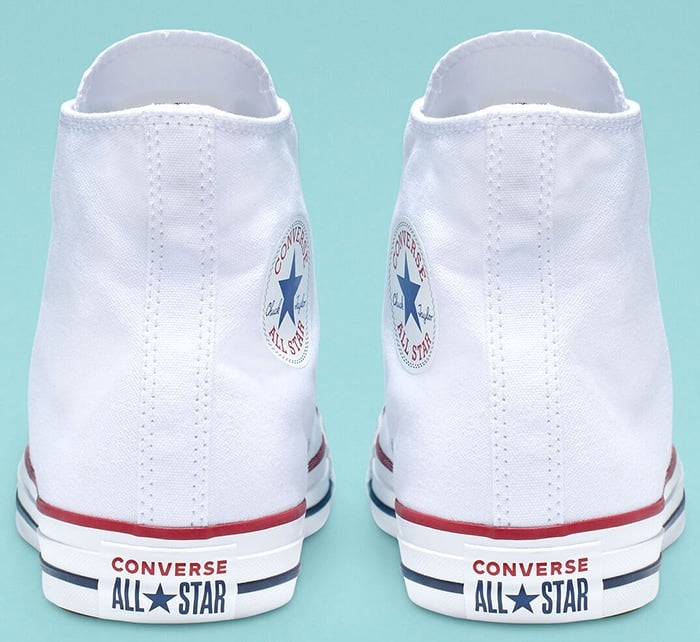 Authentic white Converse Chuck Taylor All Star sneakers featuring the signature rubber heel patch with red and navy branding