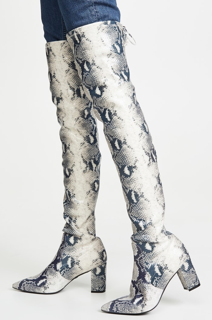 The Stuart Weitzman ‘Lesley’ over-the-knee boots feature a pointed toe, chunky block heel, and snake-print suede finish with the brand’s signature tie-back detail at the thigh