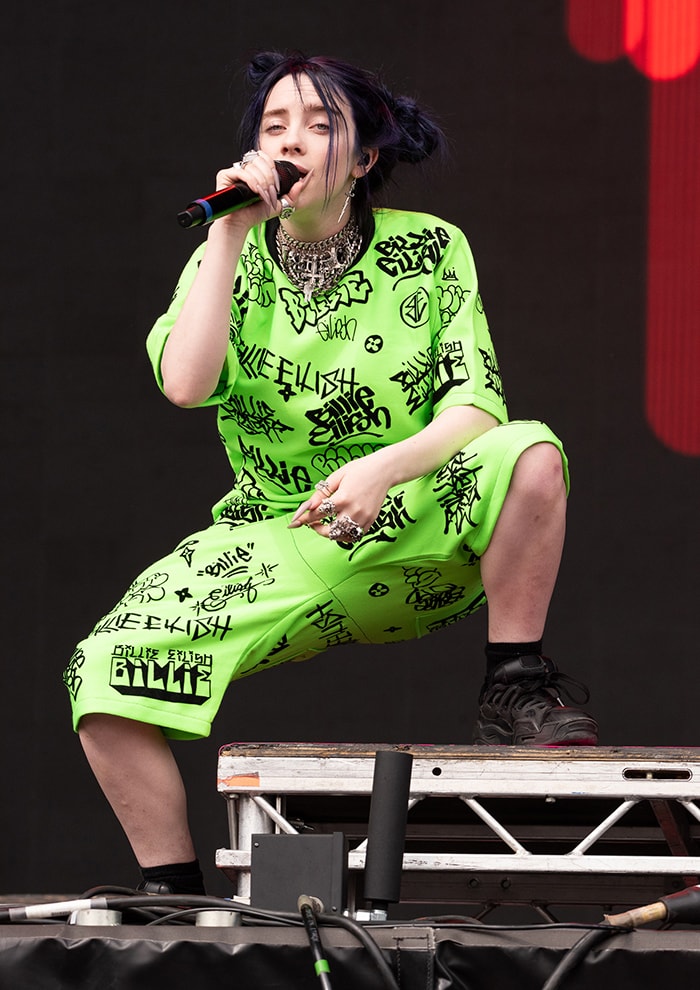 Billie Eilish performs at BBC Radio 1’s Big Weekend in a neon graffiti-print Freak City set, anchoring the oversized silhouette with Under Armour x A$AP Rocky SRLo sneakers that bring weight and attitude to the stage on May 25, 2019
