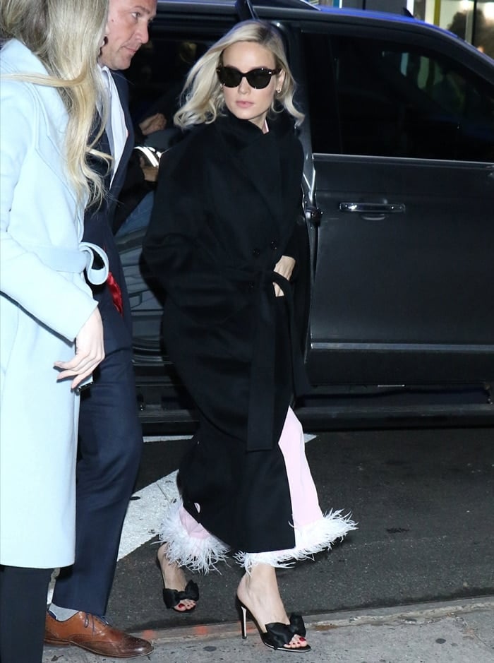 Brie Larson layered a structured black coat over Sleeper's feather-trimmed Party pajamas, revealing Giuseppe Zanotti Hanna satin mules finished with oversized bows and slender stiletto heels