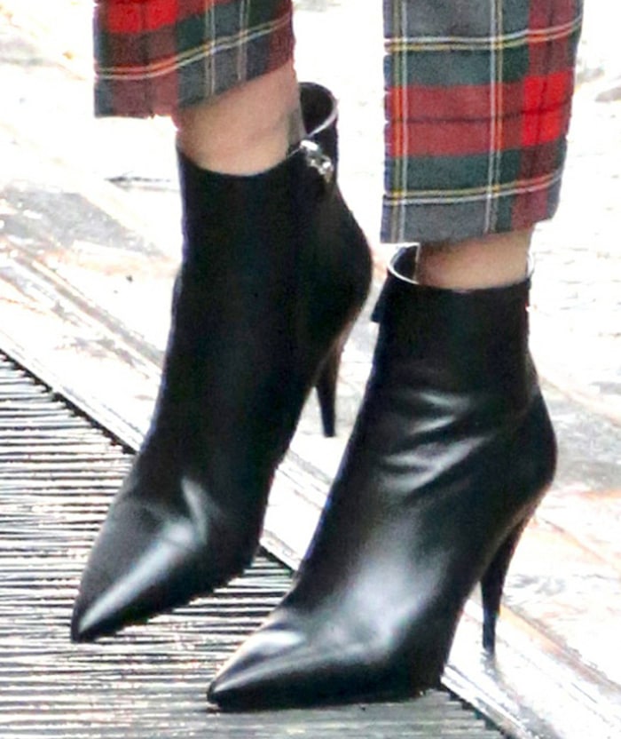 A close-up spotlights Charlize Theron’s streamlined black leather ankle boots, their pointed toes and slim heels adding polish and edge to her cropped plaid pants