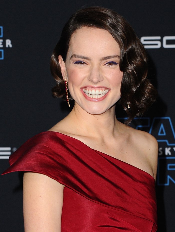 A closer look highlights the rich satin drape of Ridley’s gown and delicate ruby-and-diamond drop earrings, with the clean neckline and structured shoulder framing the polished, vintage-inspired wave set