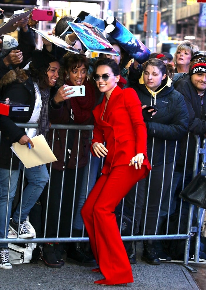 Daisy Ridley leans into the crowd in a razor-sharp red suit, the flared trousers grazing matching pointed-toe heels that extend the monochrome line into a sleek, leg-lengthening finish