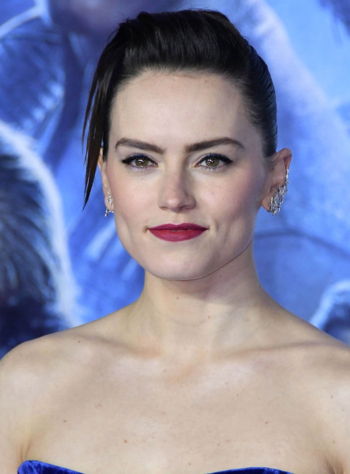 Daisy Ridley pairs her slicked-back hairstyle with plum lipstick and softly winged blue eyeliner for the European premiere appearance