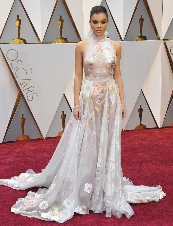 Hailee Steinfeld stuns in a hand-painted Ralph Russo gown featuring sheer floral appliqué and scalloped detailing, gracefully handling a seam rip with poise on the Oscars red carpet