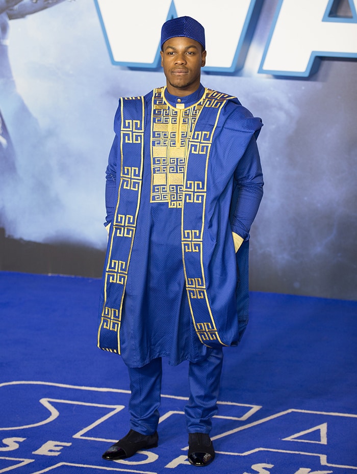 John Boyega honors his Nigerian heritage in a richly embroidered blue Agbada with a matching Fila hat and glossy black shoes
