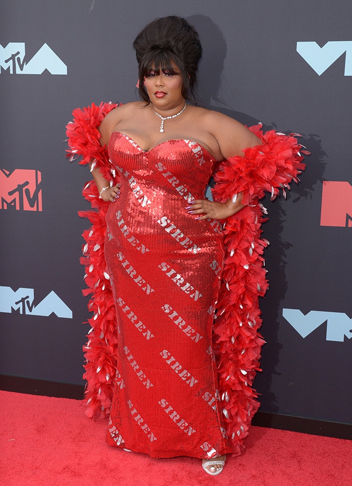 Lizzo wears a custom red sequin Moschino Siren gown with a matching feather boa and metallic red platform sandals at the 2019 MTV VMAs